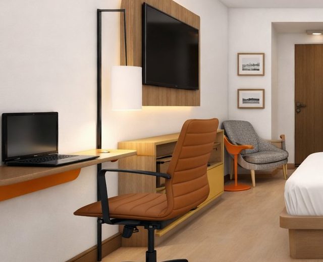 A guest room desk with an ergonomic chair and wall-mounted television